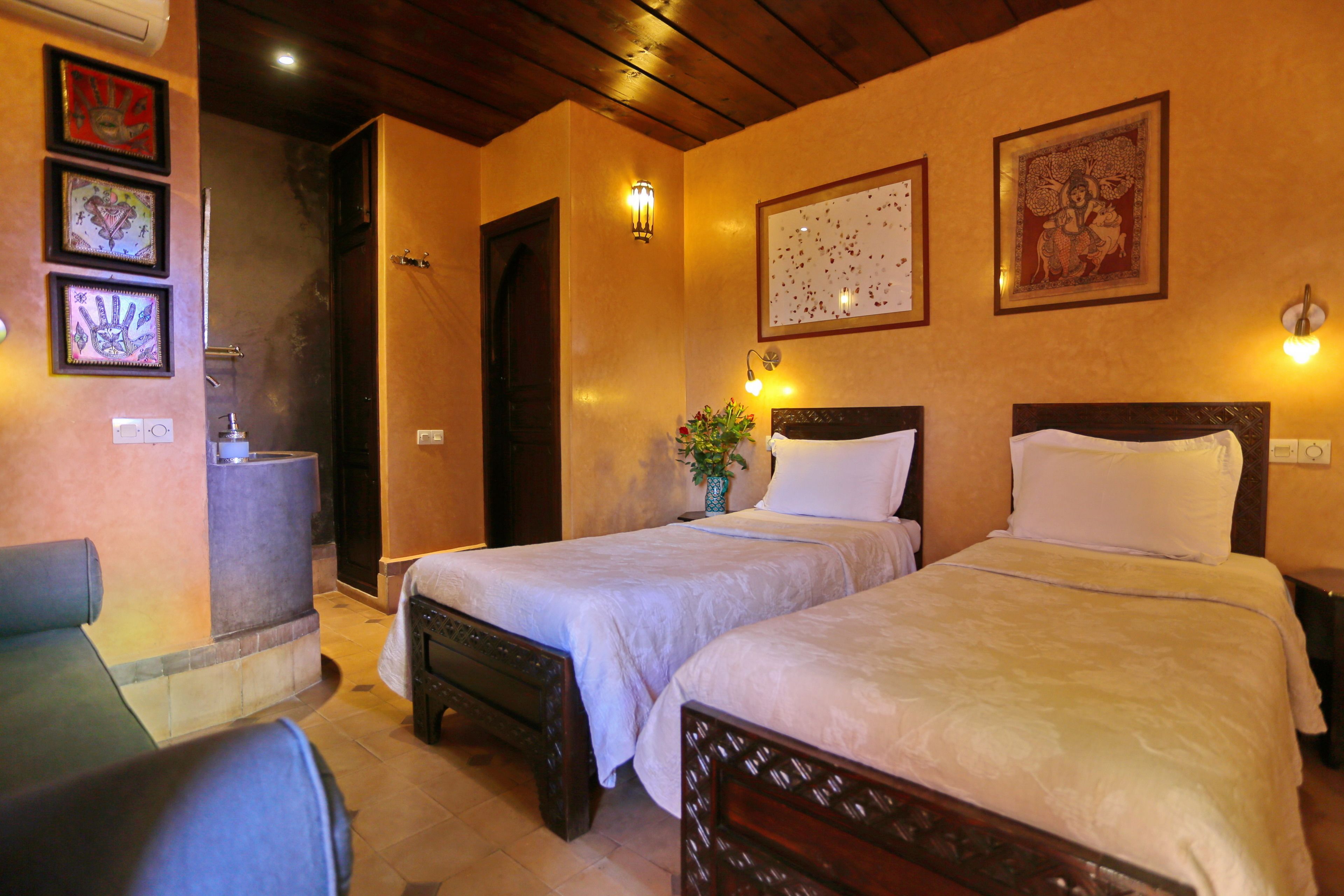 A hotel room with two single beds, a sitting area with a chair, and a small table.