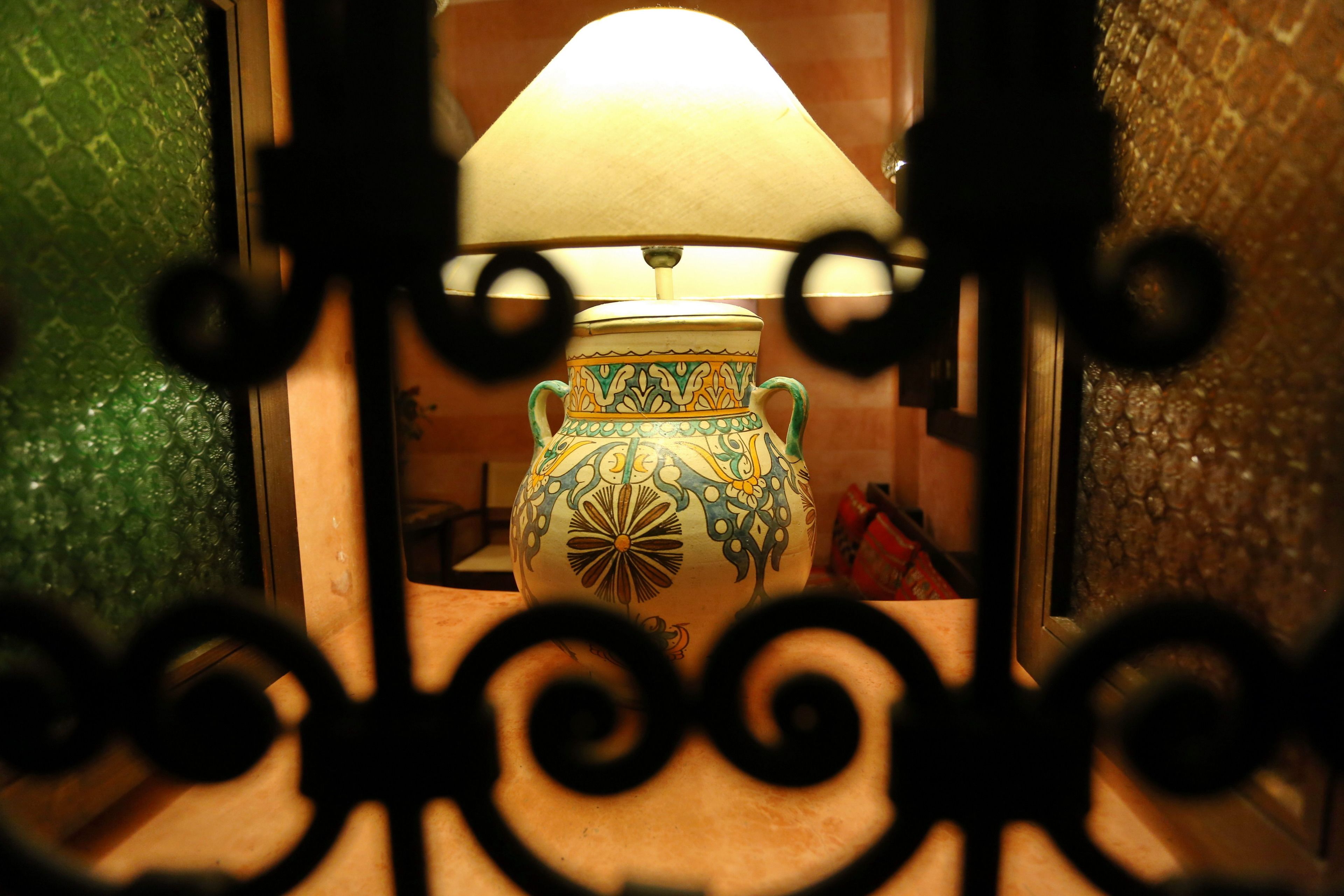 A decorative vase with a patterned design, placed in a room with a textured wall and a wooden floor.
