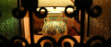 A decorative vase with a patterned design, placed in a room with a textured wall and a wooden floor.