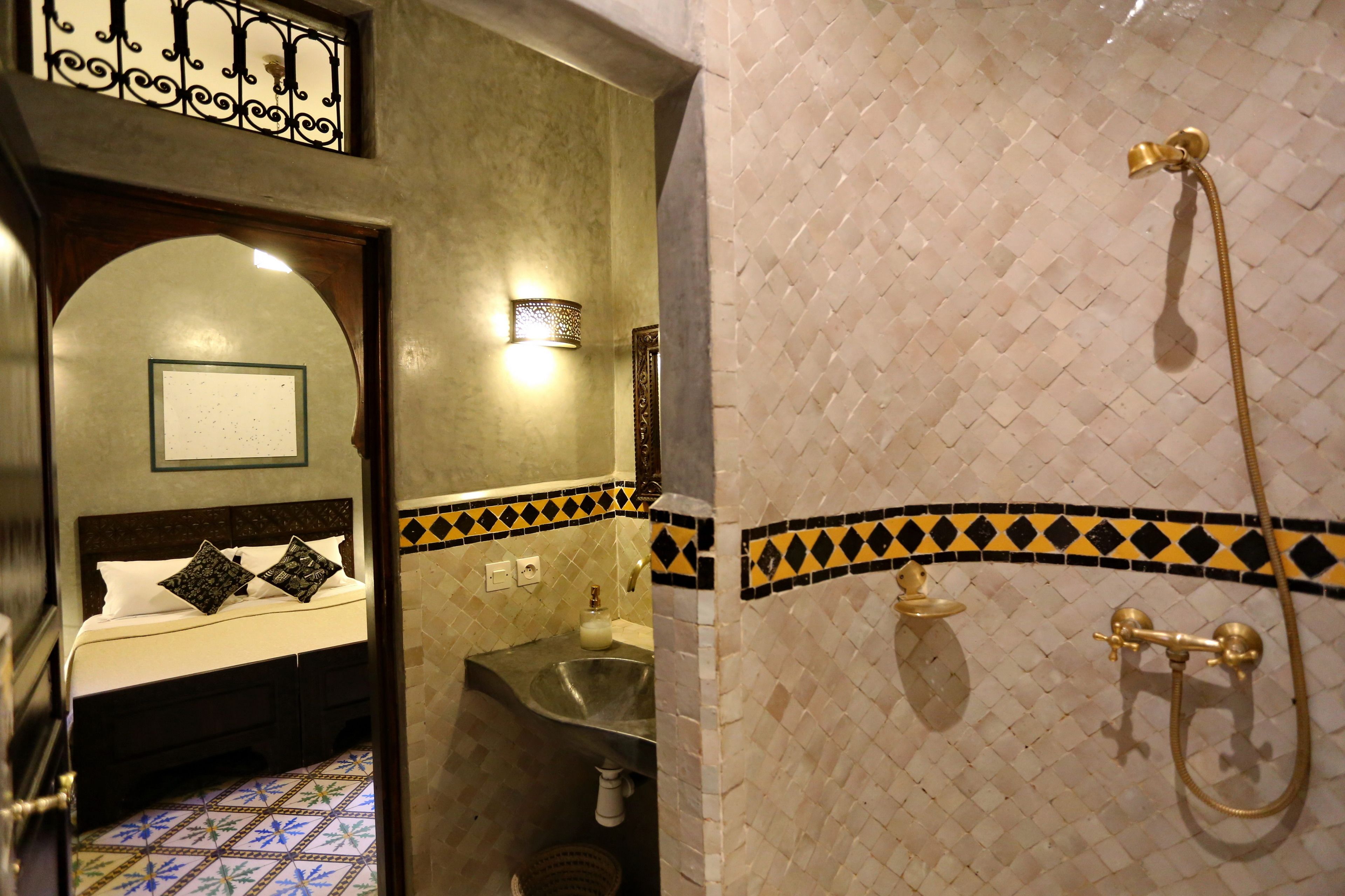 A bathroom with a shower, a sink, and a bed with decorative pillows.