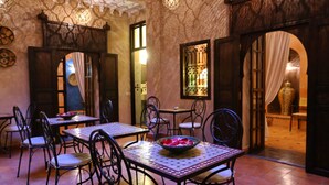 A dining area with tables and chairs, a decorative bowl on the table, and a patterned wall. - Riad Marrakiss (Marrakech)