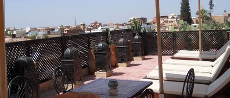 A rooftop terrace with a table, chairs, a sun lounger, and decorative elements like a cactus and metal lanterns.