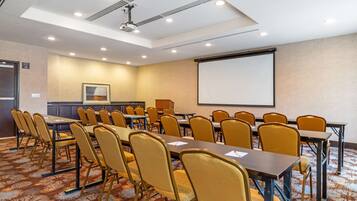 Un salón de conferencias con una pantalla de proyección grande, varias mesas y sillas.