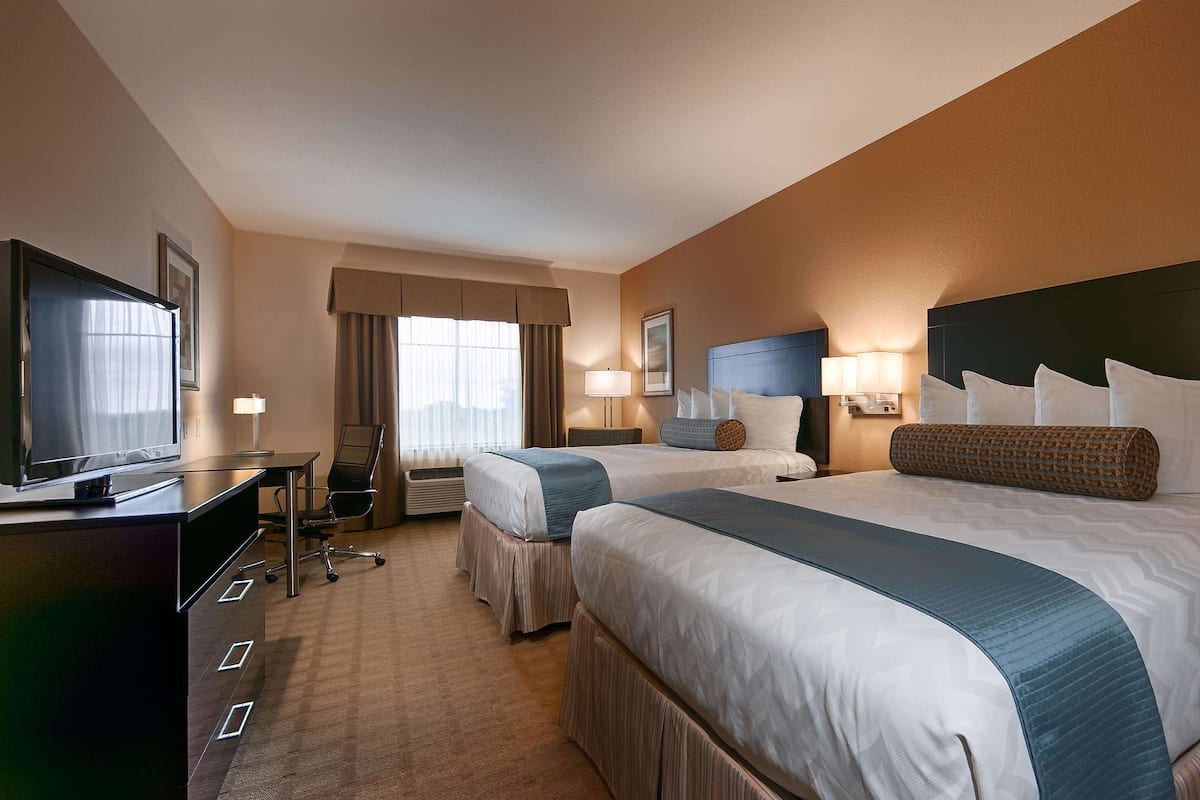 Una habitación de hotel con dos camas, un escritorio, un televisor y una ventana con cortinas.