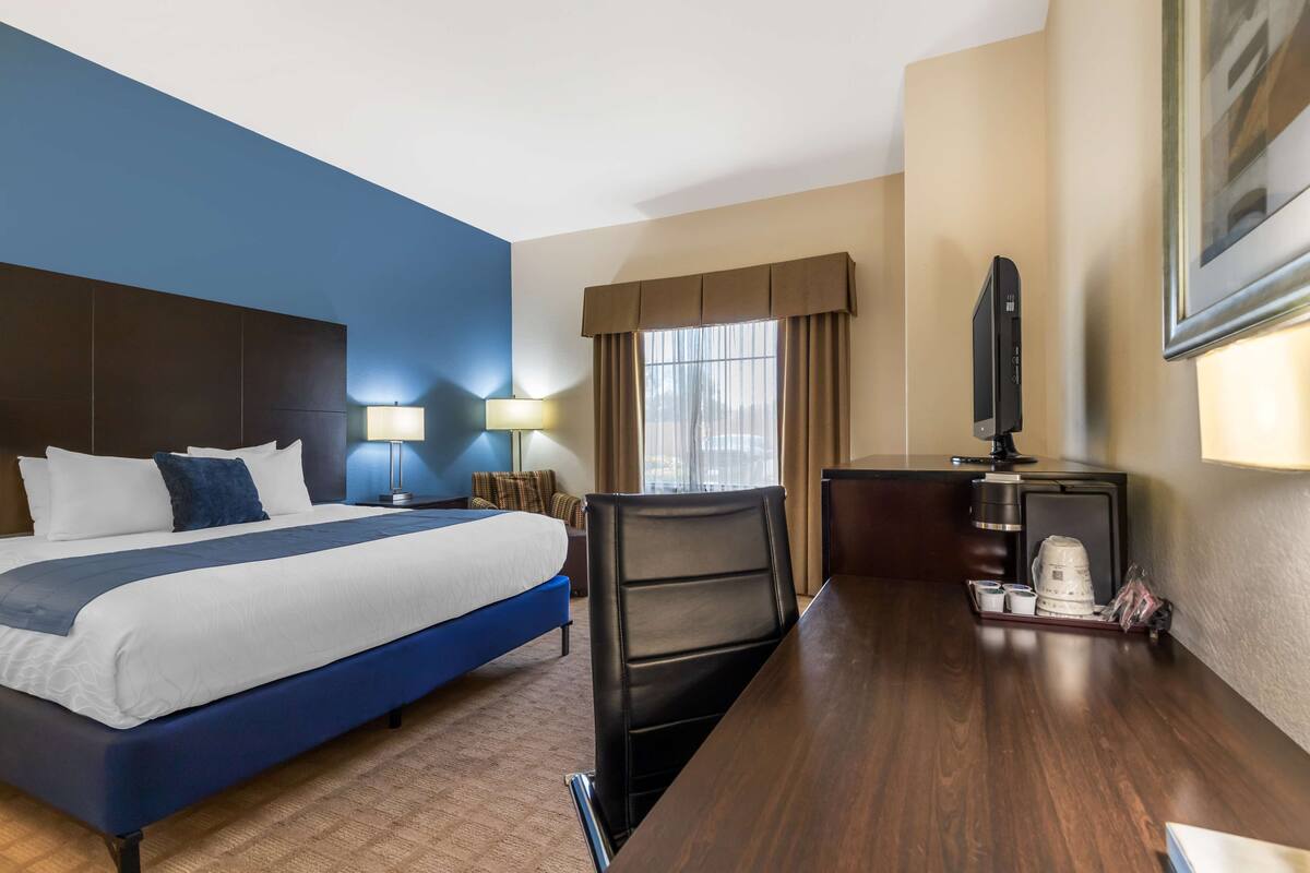 Habitación de hotel con una cama grande, un escritorio con silla, televisión y cafetera.