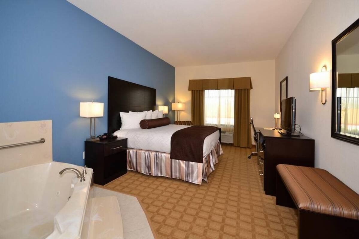 Una habitación de hotel con una cama grande, un escritorio independiente con una silla, un baño con bañera y un espejo en la pared.