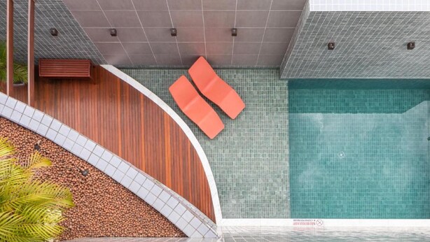 Ein moderner Poolbereich mit einer gewölbten Holzwand, zwei orangefarbenen Liegestühlen und einem gefliesten Boden.