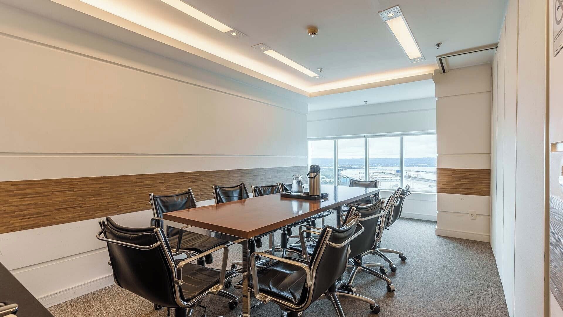 A conference room with a long table, black leather chairs, and a view through large windows.