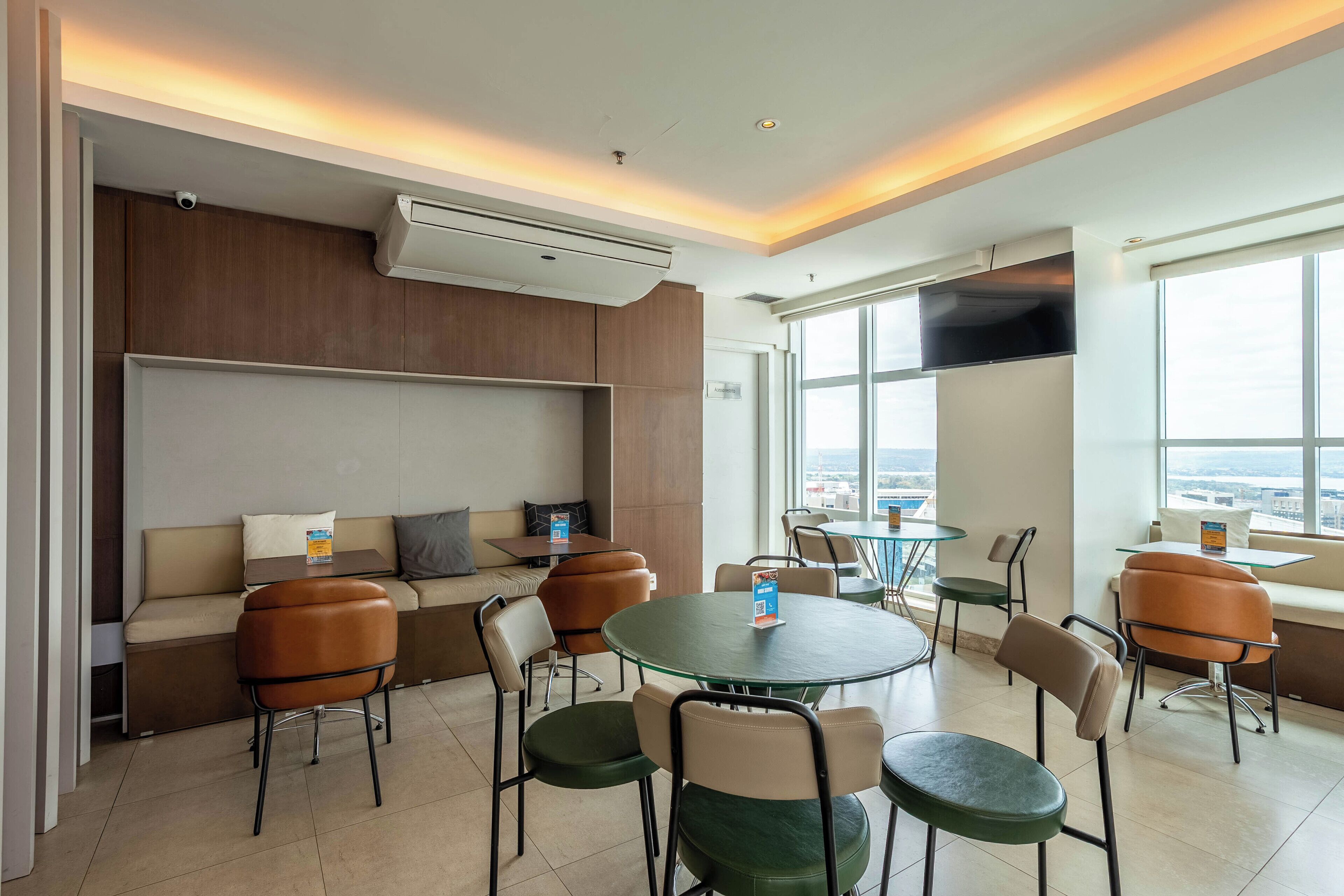 A modern hotel room with a sofa, chairs, a round table, and a TV mounted on the wall.