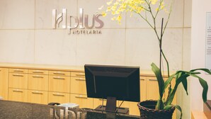 A reception desk with a computer monitor, a plant, and a sign that reads "Plus Hotelaria". - Saint Moritz Hplus Express (Brasília)