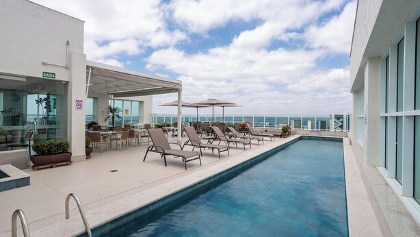 A rooftop pool with lounge chairs and a glass-enclosed area with tables and chairs. - Saint Moritz Hplus Express (Brasília)