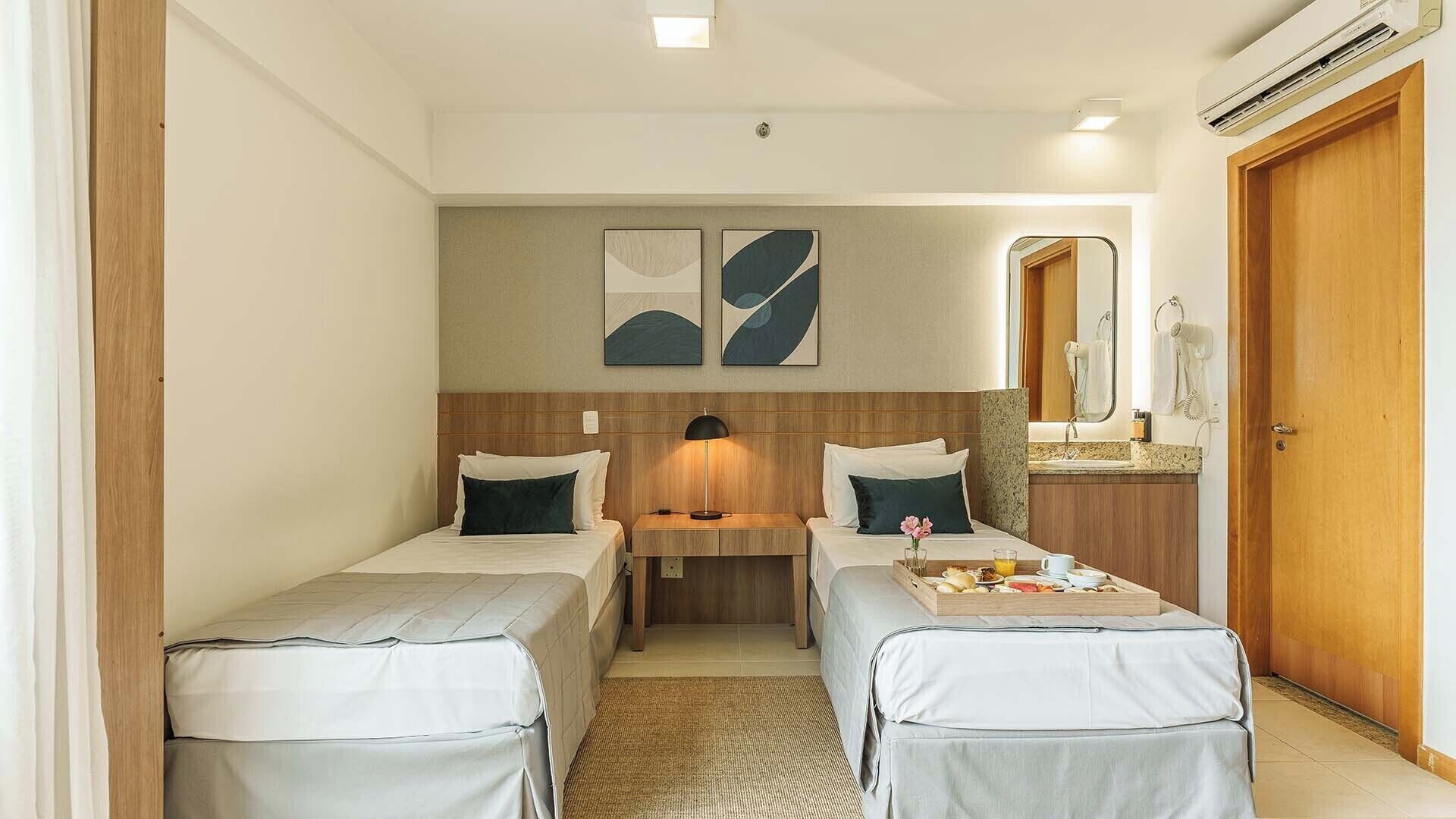 Una habitación de hotel con dos camas individuales, una mesita con desayuno, un espejo y un equipo de aire acondicionado.