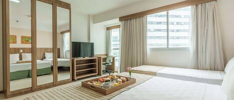 A hotel room with a large bed, a TV, a desk with a chair, a dining table with breakfast, and a window with curtains.