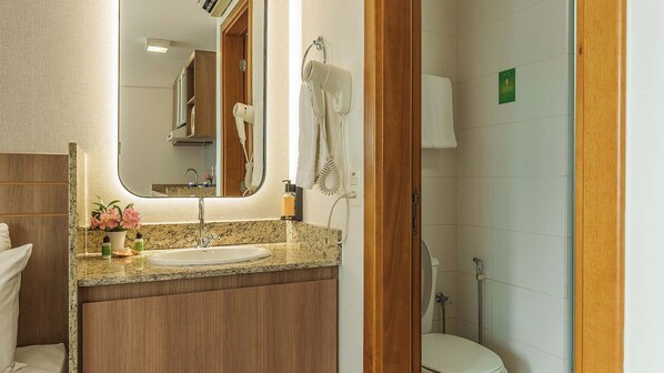 A bathroom with a granite countertop sink, a mirror, a hairdryer, and a shower.