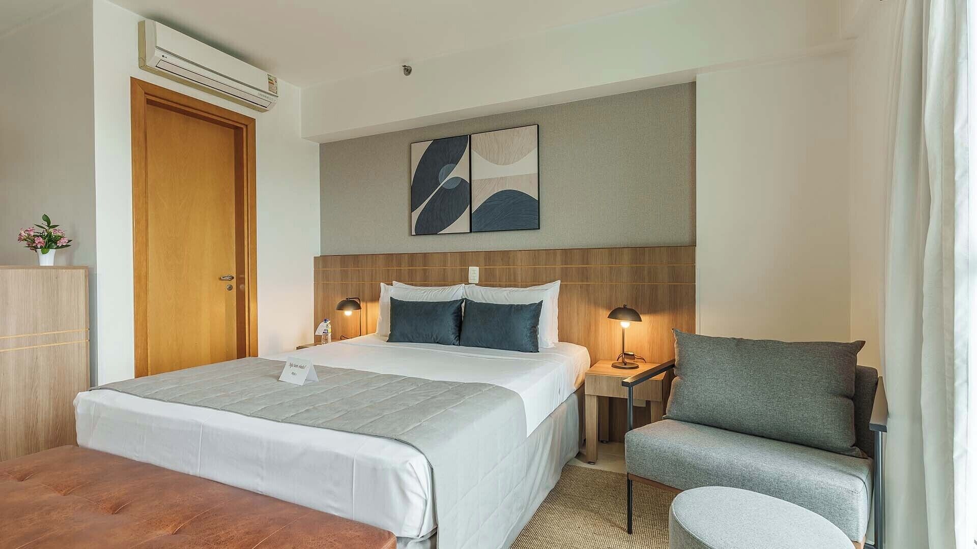 Une chambre d’hôtel avec un lit, des tables de chevet, une chaise, une lampe, un tableau et une porte en bois.