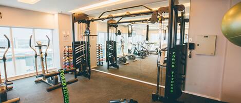 Un gimnasio con diversos equipos de ejercicio, un espejo y vistas a la ciudad a través de amplias ventanas.