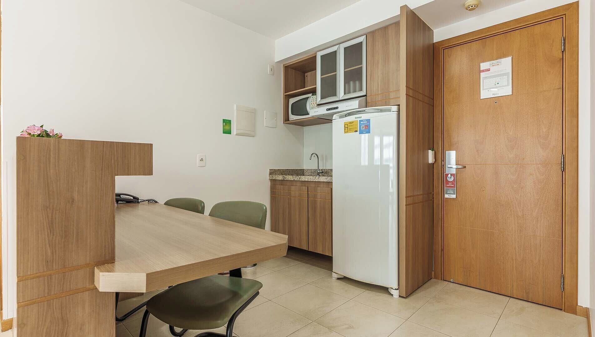 Een kleine keuken met een houten tafel, twee stoelen, een magnetron en een koelkast.