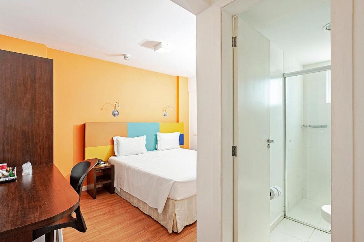 Een hotelkamer met een bed, nachtkastje en een douchehoek.