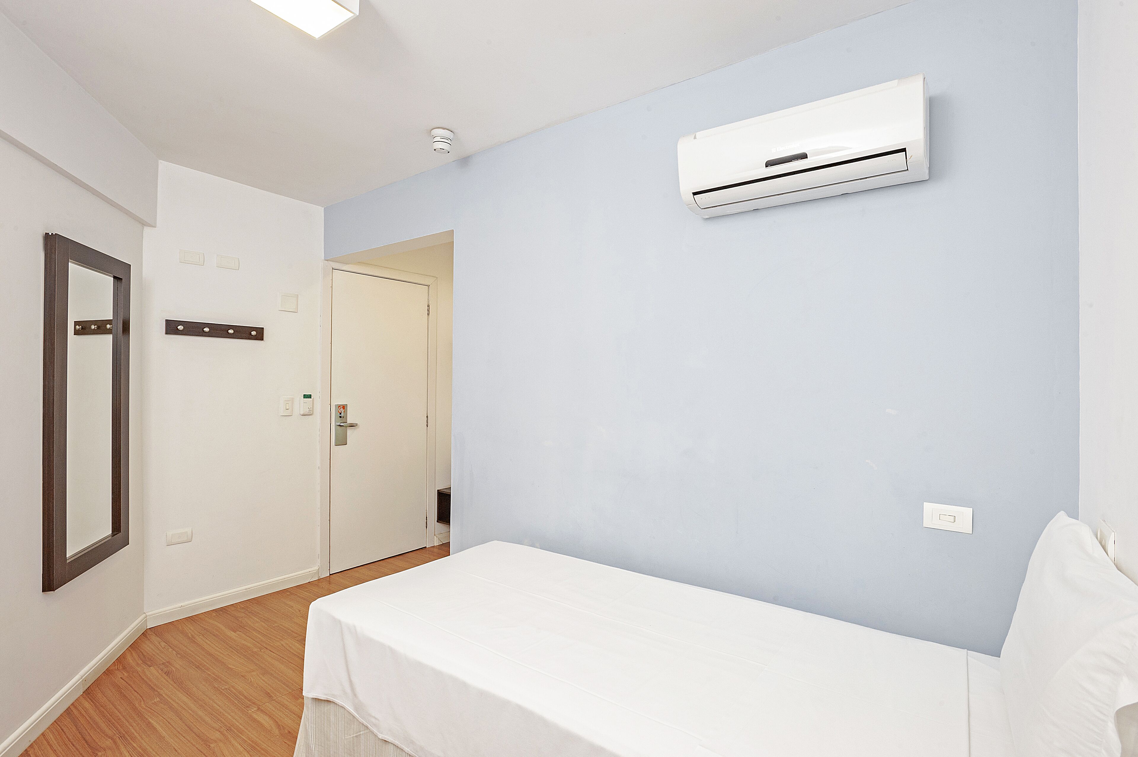 A bedroom with a bed, an air conditioning unit, a mirror, and a door.