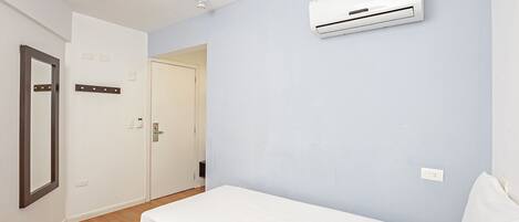 A bedroom with a bed, an air conditioning unit, a mirror, and a door.
