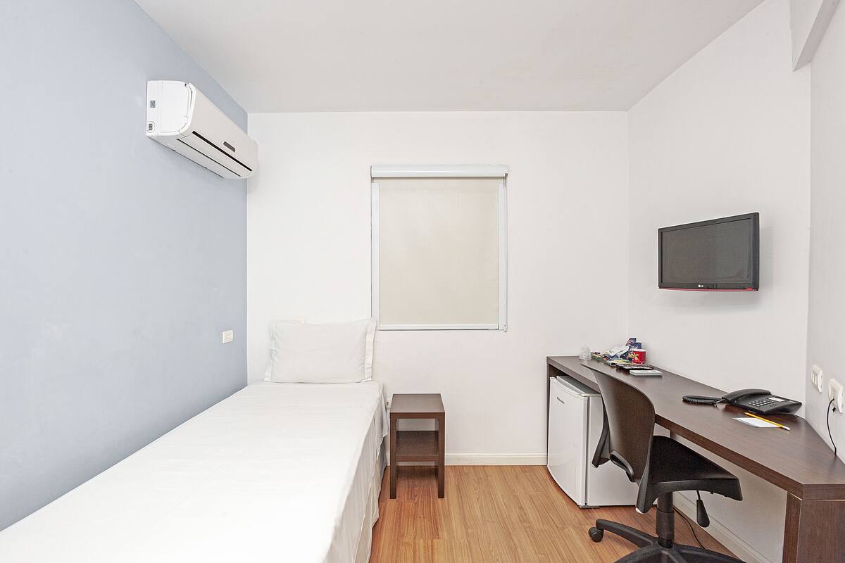 A small, modern room with a bed, desk, chair, and a television.