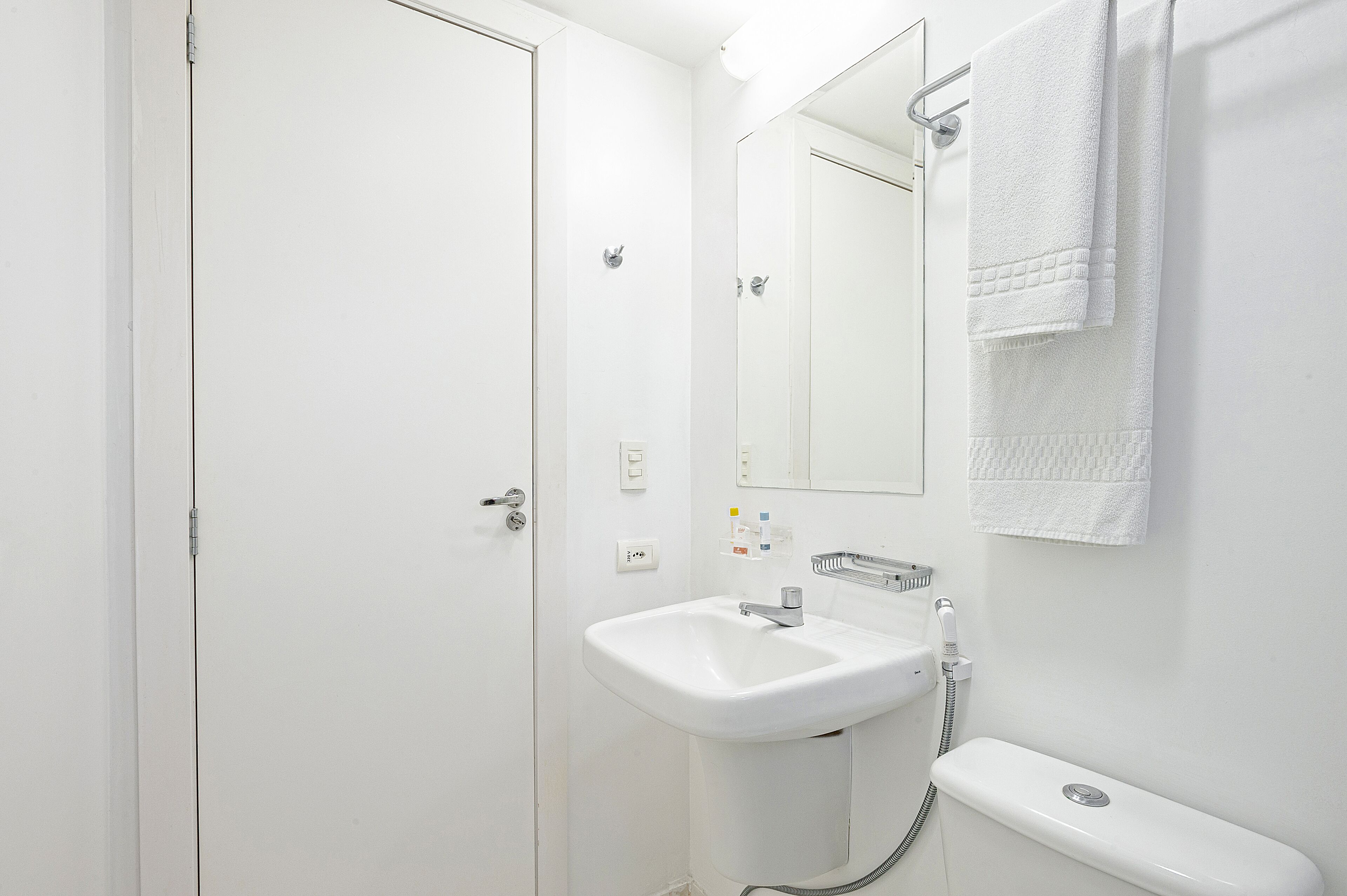 Un baño blanco con lavamanos, espejo, toallero y retrete.