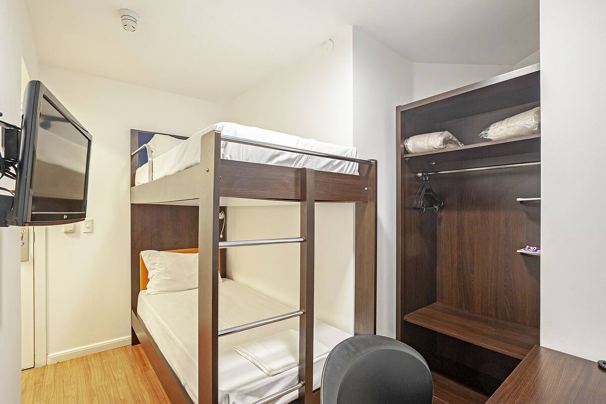 A bunk bed with a TV mounted on the wall, a wooden desk, and a wardrobe with hanging space.
