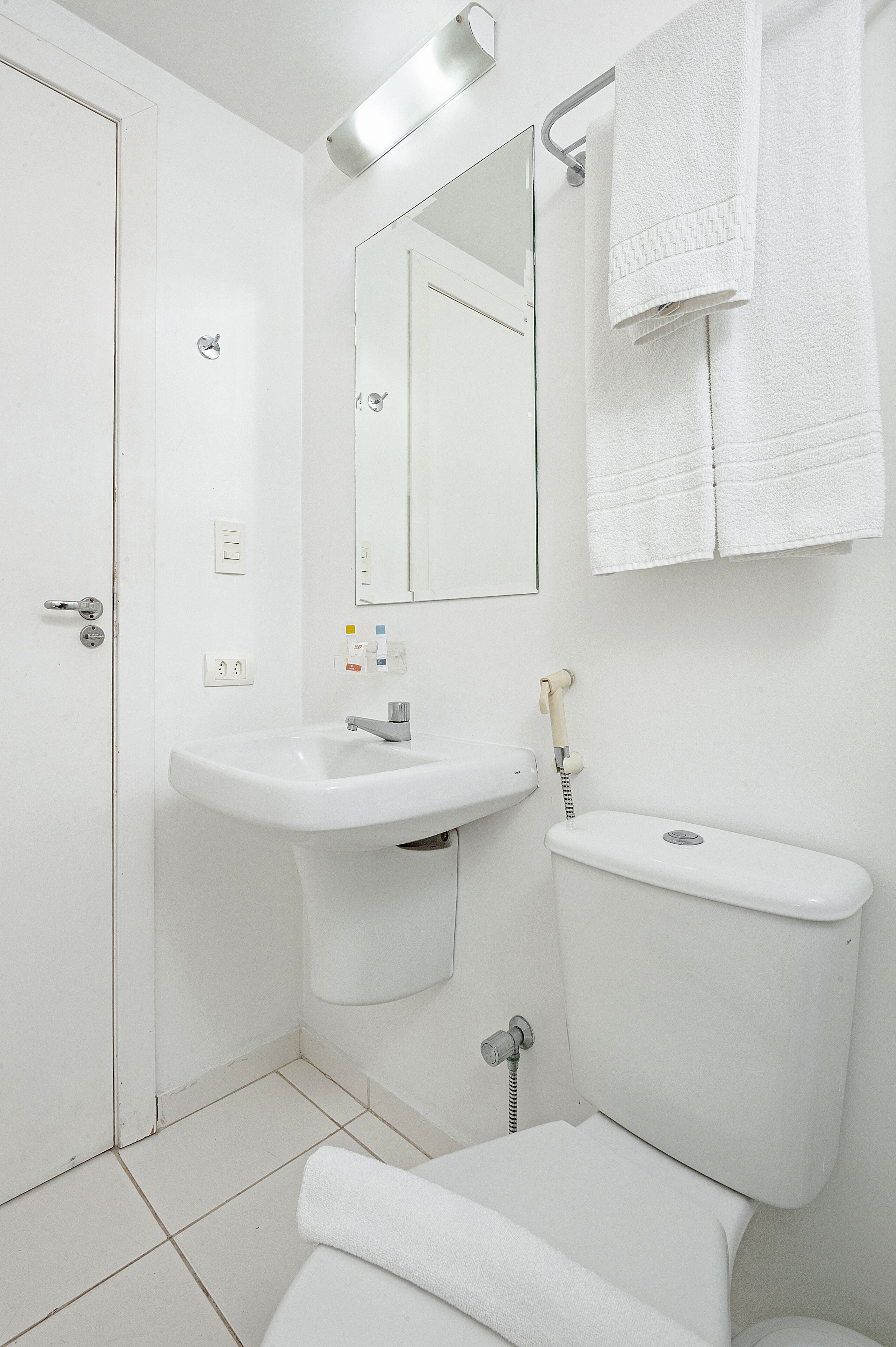 Un baño blanco con lavamanos, espejo, inodoro y toallero.