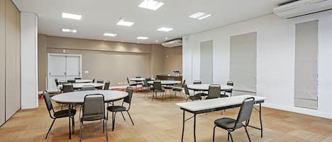 Un salón de conferencias con varias mesas y sillas, paredes blancas y piso de madera.