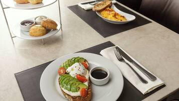 A breakfast setting with a plate of toast topped with avocado, tomatoes, and a poached egg, accompanied by a small bowl of jam and a cup of coffee.