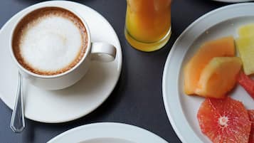 A breakfast setting with croissants, bread, eggs, bacon, toast, fruit, and a glass of orange juice.