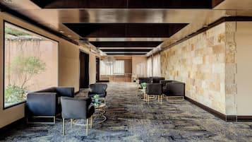 Un hall d’hôtel moderne avec un long couloir, un espace détente avec des chaises et des tables, un lustre et un mur en pierre.