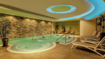 A spa area with a stone wall, a pool, lounge chairs, and a ceiling with circular lighting.