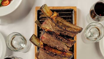 Una mesa con costillas a la parrilla, una ensalada, un recipiente con salsas, una copa de vino y una porción de papas fritas.