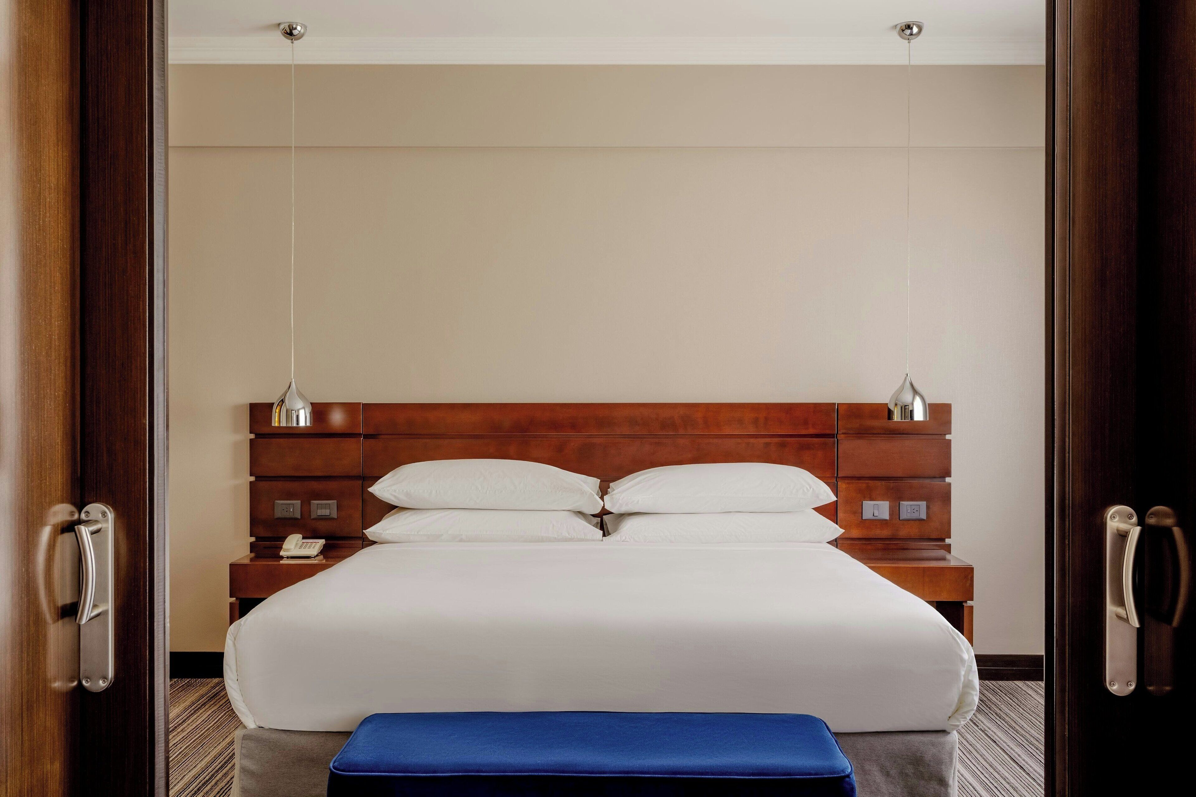 Une chambre d’hôtel avec un grand lit, une tête de lit en bois, des tables de chevet et des lampes suspendues.