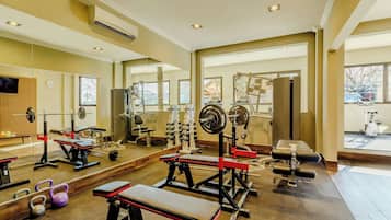 Un gimnasio con equipo de ejercicio diverso, ventanas amplias y un muro de espejos.