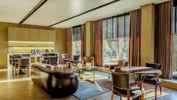 Una sala de estar moderna con un sofá, sillas, una mesa de centro y un comedor. Se observa una cocina al fondo con armarios y electrodomésticos.