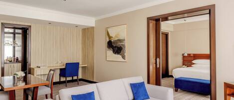A hotel room with a sofa, a dining table, a chair, a bed, and a painting on the wall.