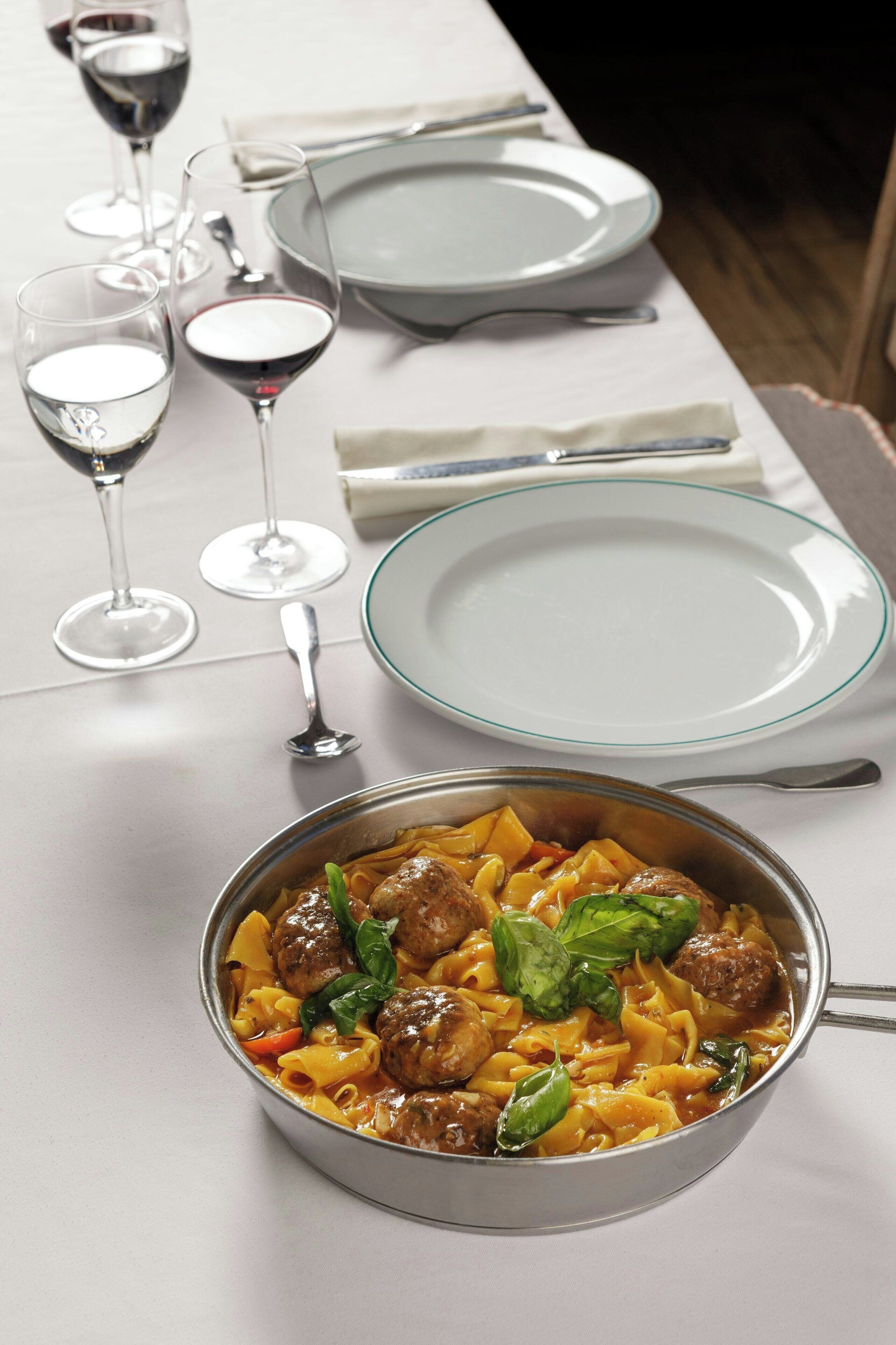 Una tavola imbandita con piatti, bicchieri e una ciotola di pasta con polpette.