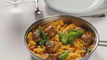 A dining table set with plates, glasses, and a bowl of pasta with meatballs.