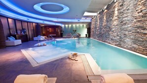 Zona d'una piscina interior moderna amb pared de pedra, gandules i taulell de recepció.