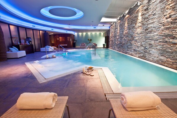 Un área de piscina interior moderna con pared de piedra, sillones de descanso y un mostrador de recepción.