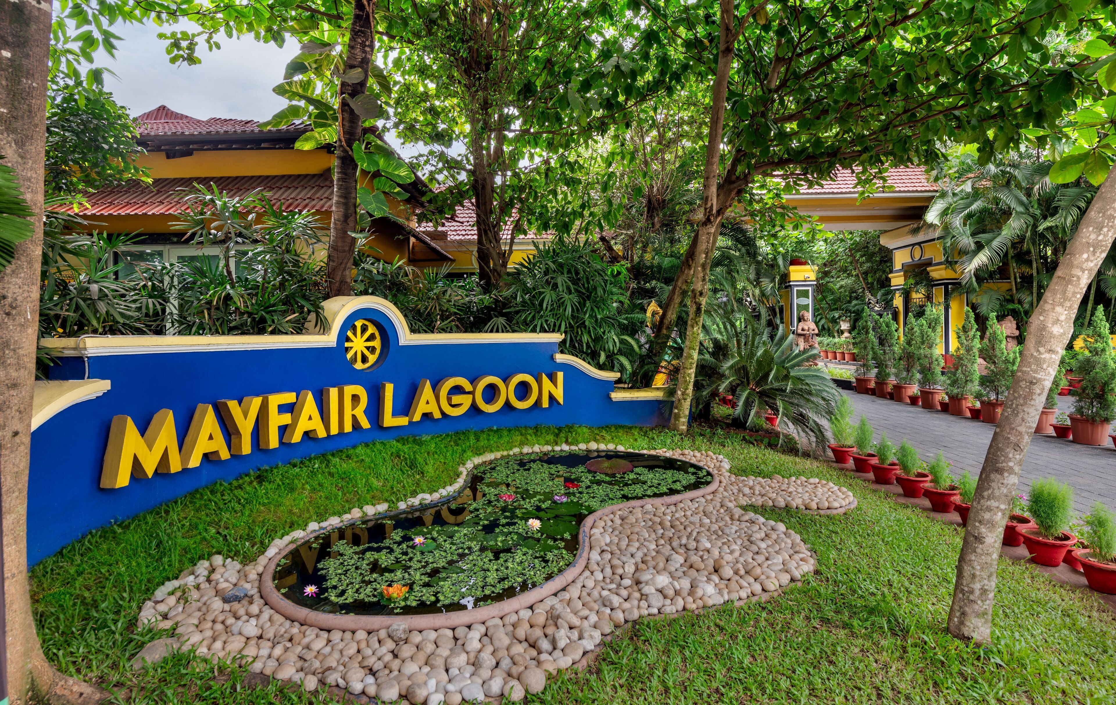A sign for Mayfair Lagoon with a water feature and potted plants.