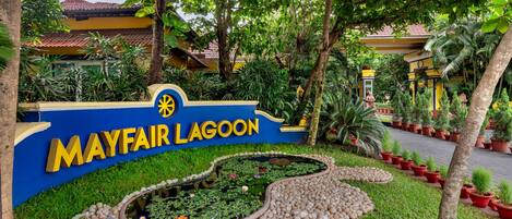 A sign for Mayfair Lagoon with a water feature and potted plants.