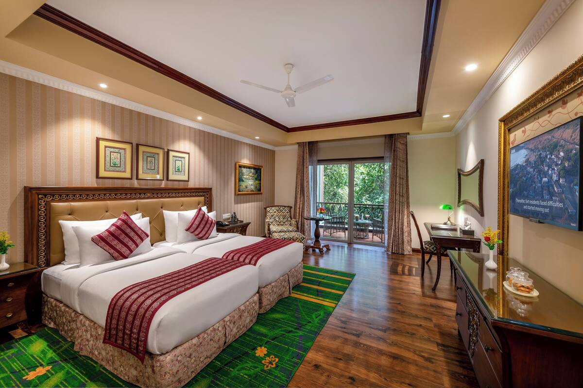 A hotel room with a large bed, a desk, a chair, a balcony with a view, and framed pictures on the wall.