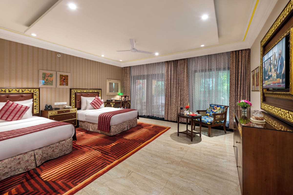 A hotel room with two beds, a desk, a chair, a TV, and a large window with curtains.