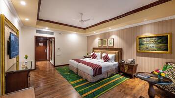 A hotel room with a large bed, a dining table, a sofa, and a ceiling fan.