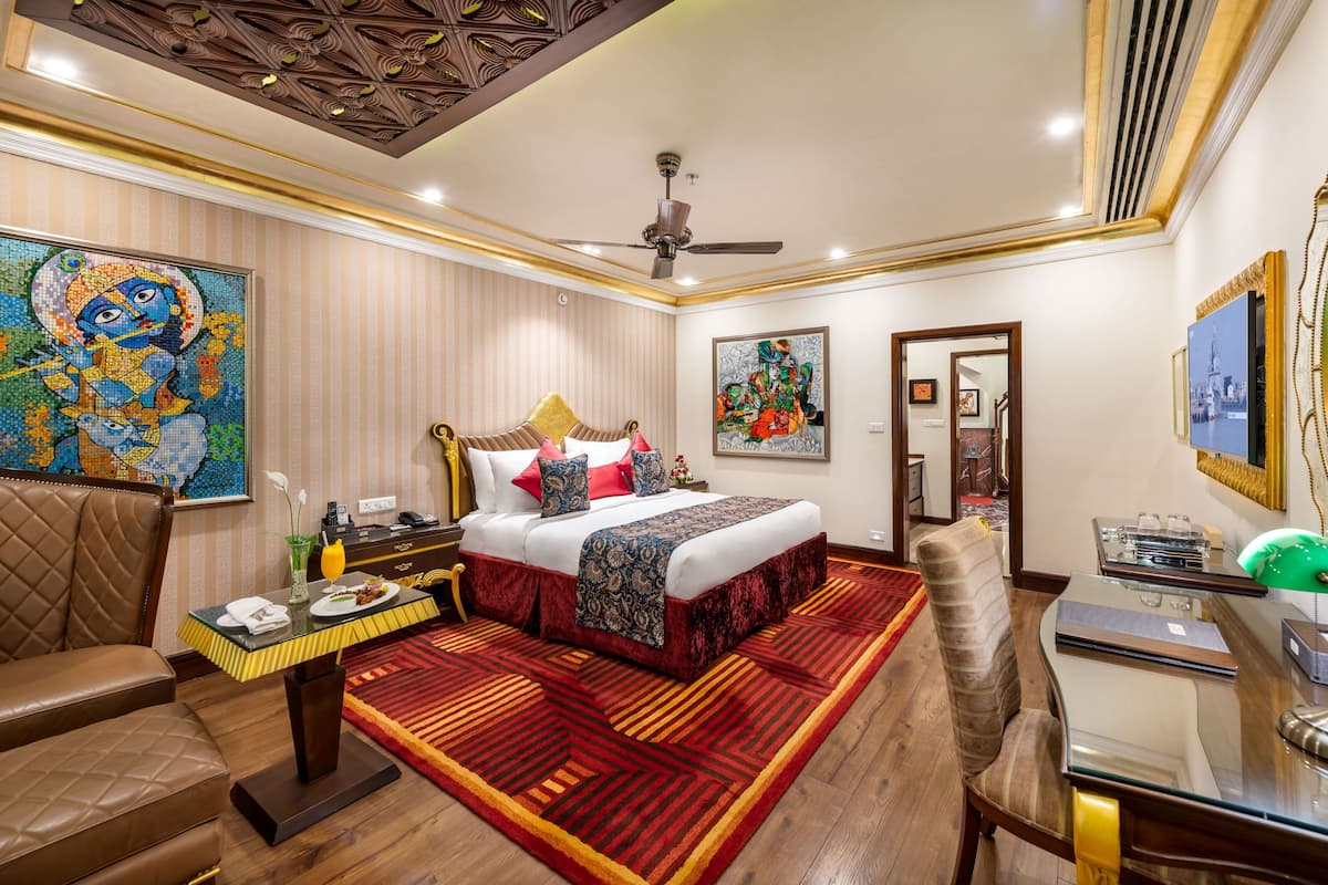 A hotel room with a large bed, a desk, a chair, a sofa, and a ceiling fan.