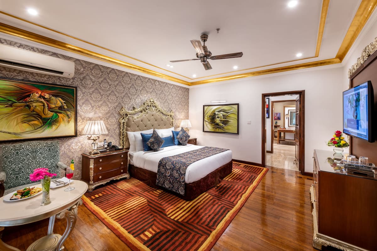 A hotel room with a large bed, a desk with a chair, a TV, and a decorative wall.