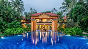 A large, luxurious pool with a tiled floor, surrounded by lush greenery and a grand building with a red roof. - Mayfair Lagoon (Bhubaneshwar)